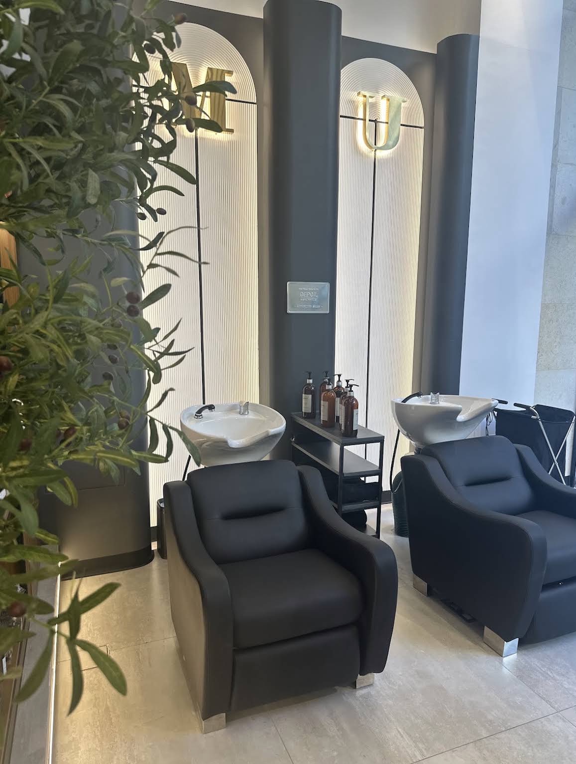 Backwash chairs beneath the backlit gold M and U lettering at Volume Gentlemen Barber & Spa