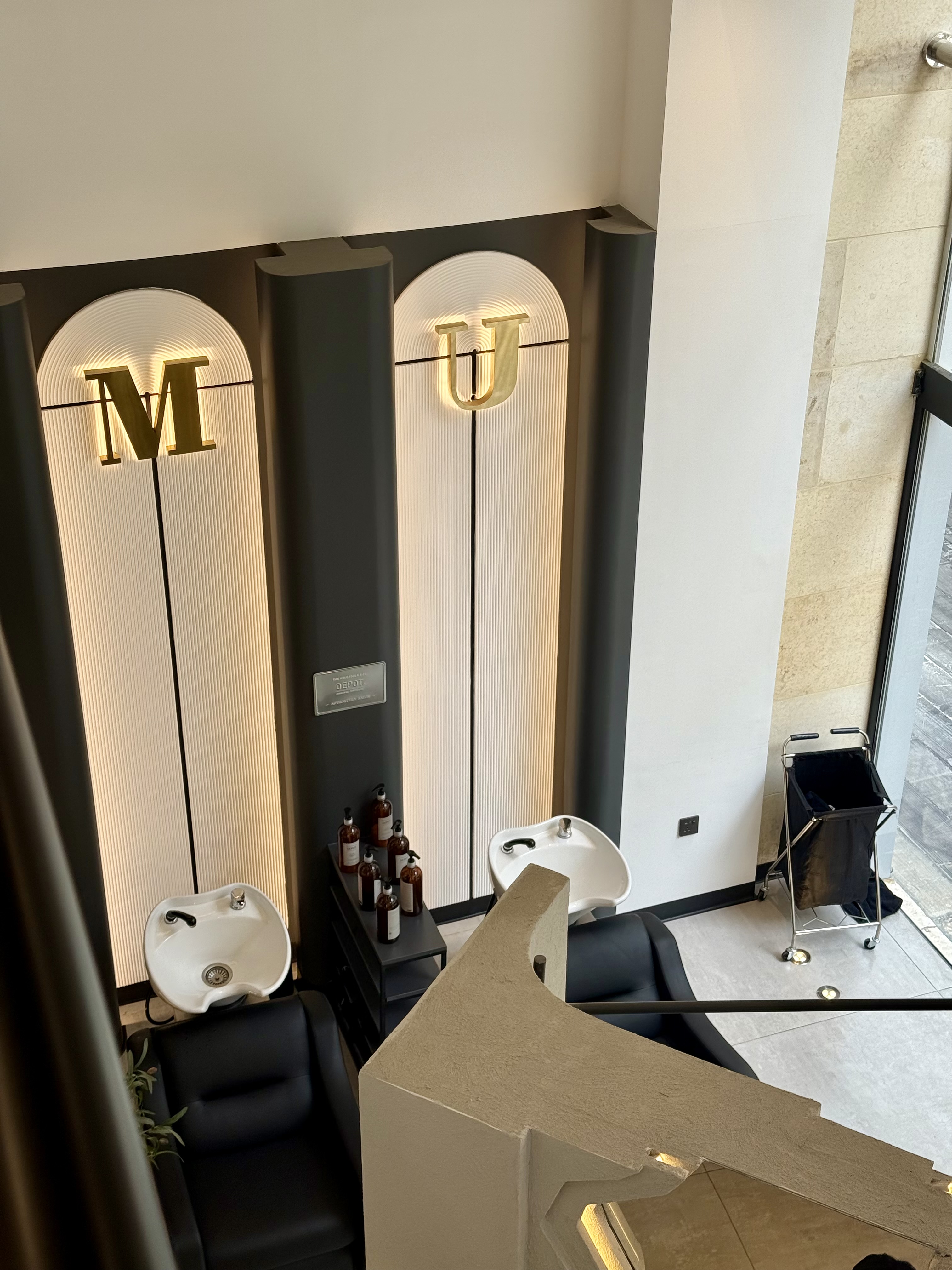 Backwash stations beneath backlit arches with brass M and U lettering