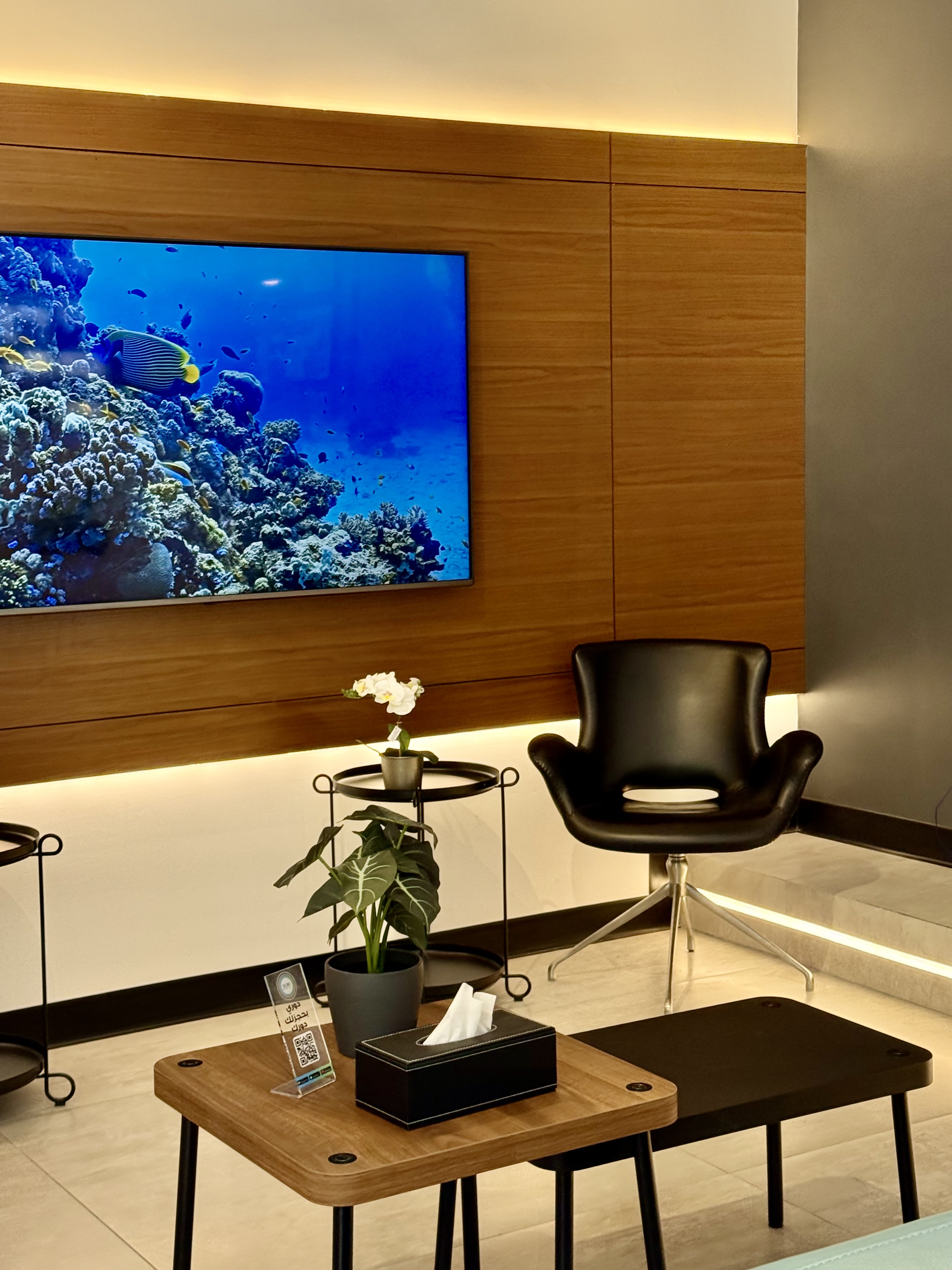 Lounge seating with a wall-mounted screen, orchid and designer chair at Volume Gentlemen Barber & Spa
