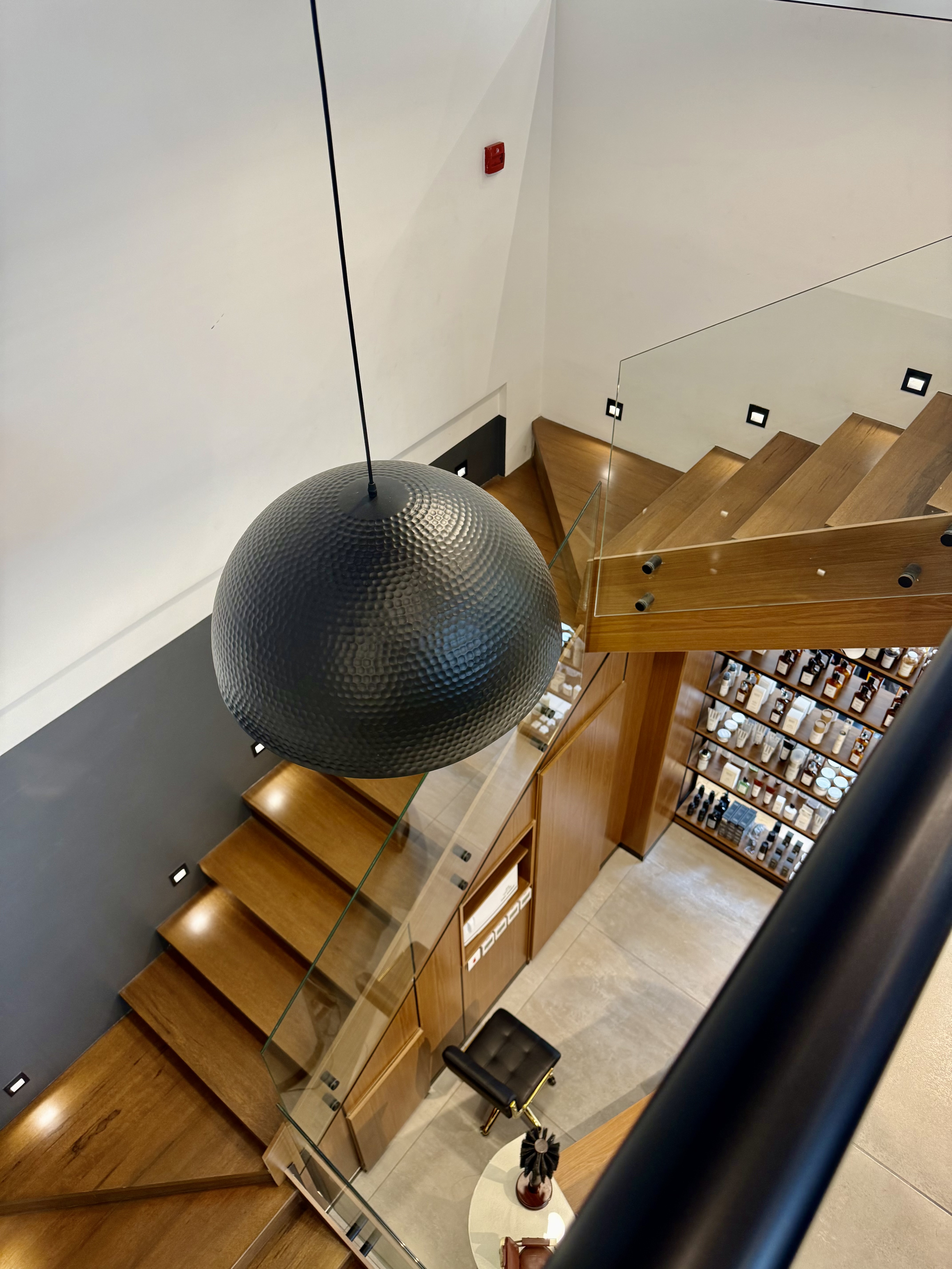 Double-height stairwell with a sculptural pendant light above the product wall